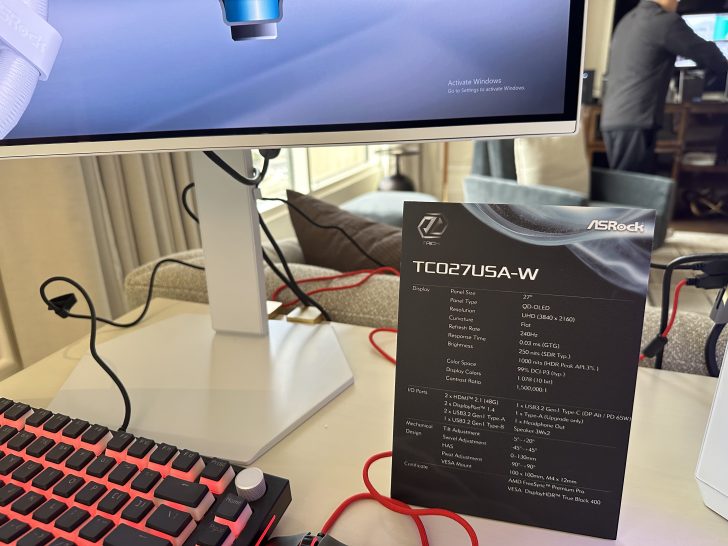 An ASRock TC027USA-W monitor displaying an activation message with detailed specifications on a nearby sign, including a 27 QD-OLED panel and 240Hz refresh rate.