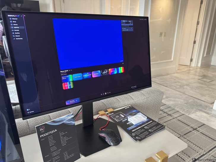 A display shows the ASRock PGQ27Q5A monitor running the SignalRGB app with the 'Neon Shift' effect, alongside a brochure and gaming mouse.