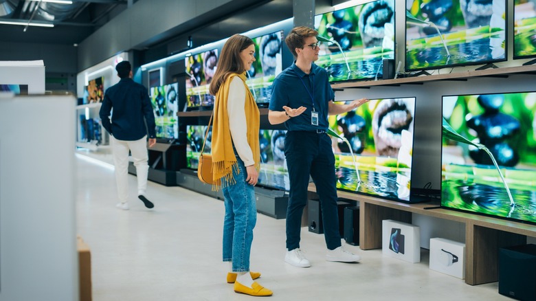 Συνεργάτης πωλήσεων που δείχνει τηλεοράσεις στον πελάτη στο κατάστημα.