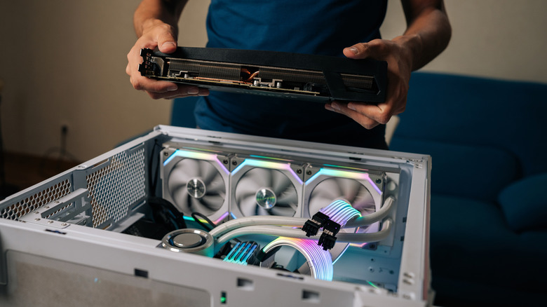 Άτομο που κρατά μια κάρτα γραφικών πάνω από μια ανοιχτή θήκη επιτραπέζιου υπολογιστή