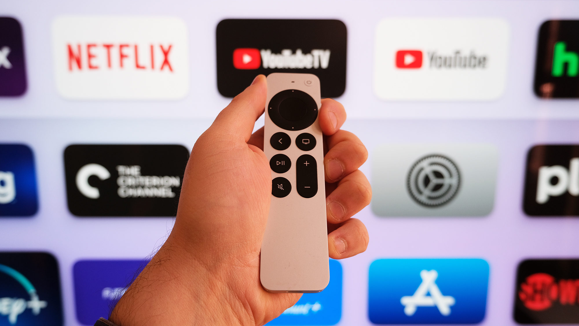 Το τηλεχειριστήριο Apple TV 4K (2022) μπροστά από μια τηλεόραση με την αρχική οθόνη tvOS.