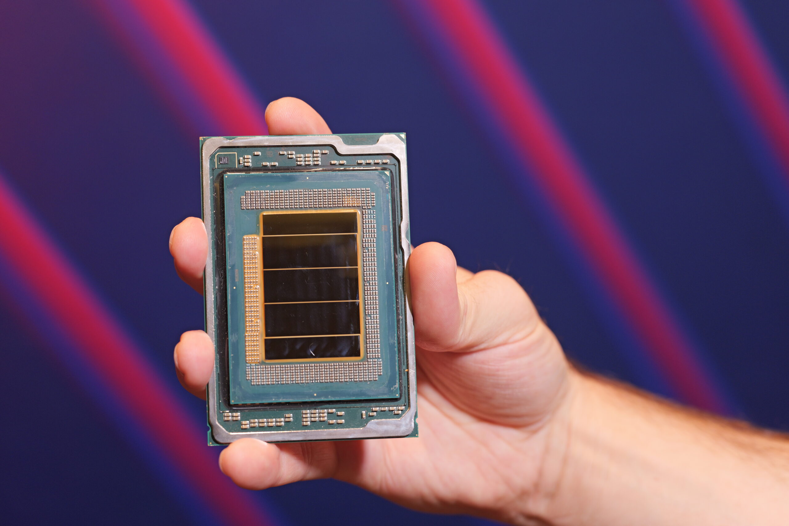 Ένα άτομο που κρατά έναν επεξεργαστή Intel με ορατή μήτρα και περίπλοκα κυκλώματα, σε θολό φόντο με διαγώνιο