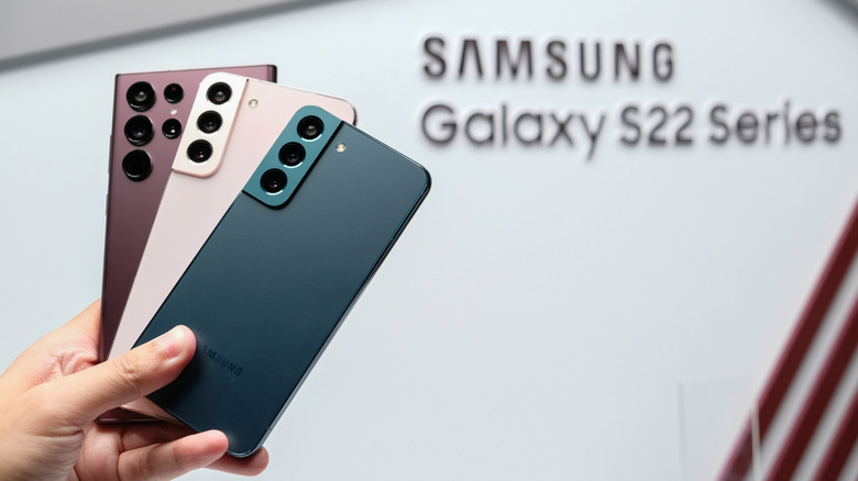 Κάποιος κρατά ψηλά τα τηλέφωνα της σειράς Samsung Galaxy S22 μπροστά από το λογότυπο.