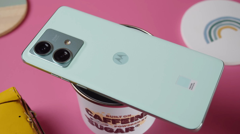 Ένα ανοιχτό πράσινο smartphone Motorola πάνω από ένα φλιτζάνι καφέ, σε ροζ φόντο.